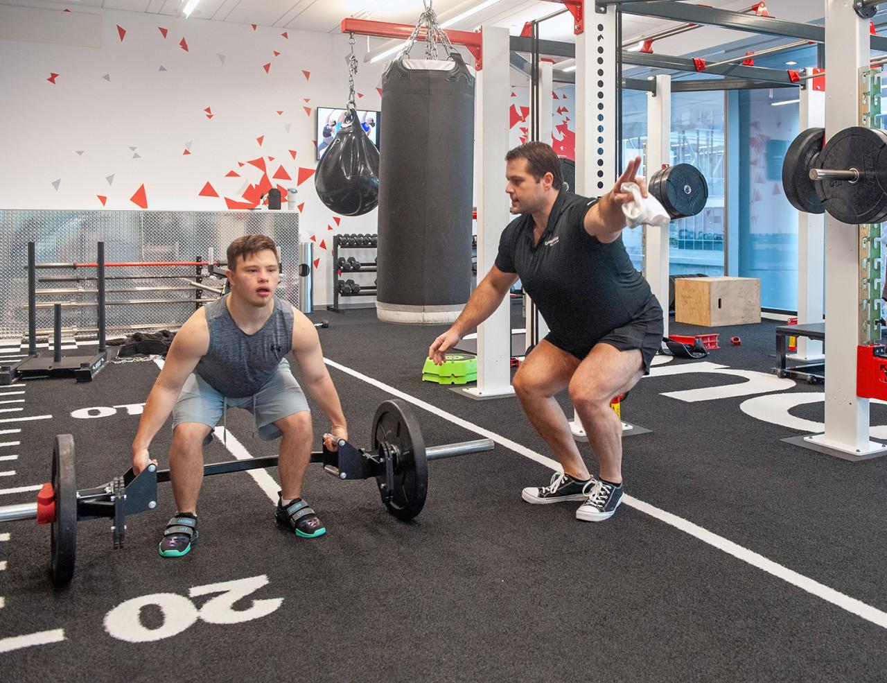 A young man coached through a deadlift in a gym